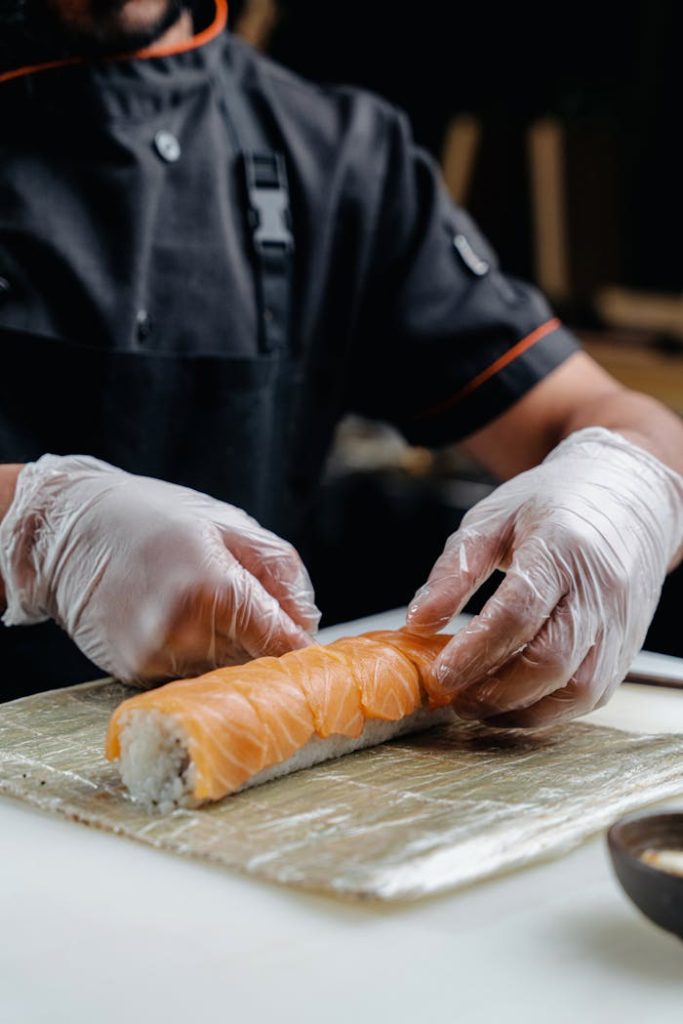 Expert chef rolls delicate salmon sushi with professionalism, showcasing food preparation artistry.